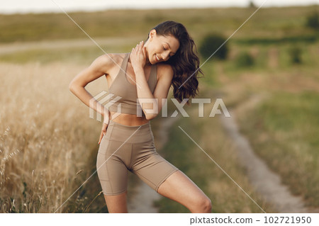 Pretty lady training in a summer field. Brunette doing yoga. Girl in a sportsuit. 102721950