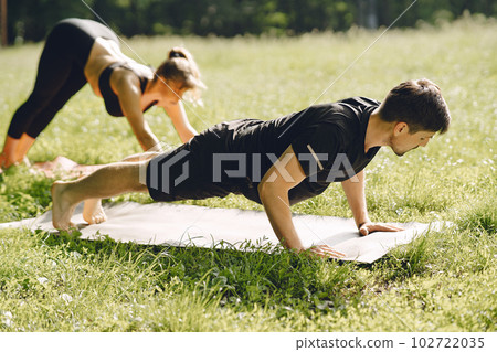 Young sportive couple doing yoga fitness . People in a summer park. 102722035