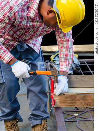 Man hammering a nail into the wooden board. 102723047