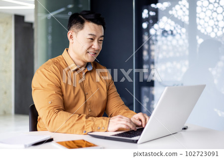 Cheerful and smiling Asian man working inside office, businessman in shirt and glasses using laptop, engineer developer programmer typing code programming software 102723091