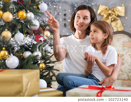 Mom and daughter holding Christmas decorations on Christmas tree Mom and daughter holding Christmas decorations on Christmas tree 102723140