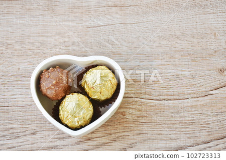 chocolate ball wrapped in gold foil packaging in heart bowl on table chocolate ball wrapped in gold foil packaging in heart bowl on table 102723313