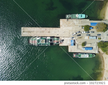 Ferry boat crossing the sea, carrying cars and passengers. Cars drive off the deck onto the port. Top-down aerial drone view Ferry on the lake, transporting cars: deck of a boat carrying vehicles. Ferry boat crossing the sea, carrying cars and passengers. Cars drive off the deck onto the port. Top-down aerial drone view Ferry on the lake, transporting cars: deck of a boat carrying vehicles. 102723921
