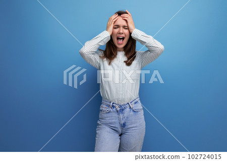 upset young brunette lady wearing striped shirt and jeans holding her head and screaming 102724015
