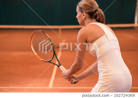 View from the back on a female tennis player on a court indoor View from the back on a female tennis player on a court indoor 102724369
