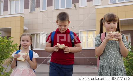 small children eat sandwiches. full child concept. boy girl have breakfast sandwich bread sausage cheese together. school friends with backpacks recess school yard. happy childhood. healthy eating 102727530