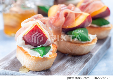 Delicious prosciutto peach bruschetta. Crostini, cream cheese, basil, peach, prosciutto, horizontal 102728478