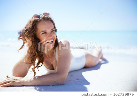 happy modern woman in white beachwear laying at beach 102729979