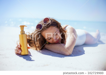 relaxed stylish female in white swimwear laying at beach 102729980