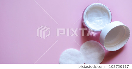 an open jar with cream and lid on a pink background, body and face cream, cotton swabs, a beauty salon banner, a frame with a place for text an open jar with cream and lid on a pink background, body and face cream, cotton swabs, a beauty salon banner, a frame with a place for text 102730117