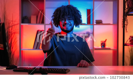 Like gesture. Positive answer. Happy man. Smiling guy showing thumb up sitting desk with keyboard in dark neon light home interior. 102730843