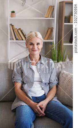 Happy woman. Enjoying rest. Home leisure. Smiling female sitting sofa in light home interior. 102730984