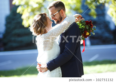 Couple enjoying romantic moments in park. Elegant bride in beautiful white dress, groom in a suit. 102731132