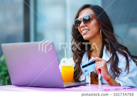 Young woman sitting at cafe making online shopping, using credit card and laptop. Online shopping. Young woman sitting at cafe making online shopping, using credit card and laptop. Online shopping. 102734788