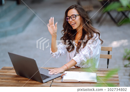 Young woman with wireless headphones calling on laptop, talk by webcam, video conference on cafe. Young woman with wireless headphones calling on laptop, talk by webcam, video conference on cafe. 102734802
