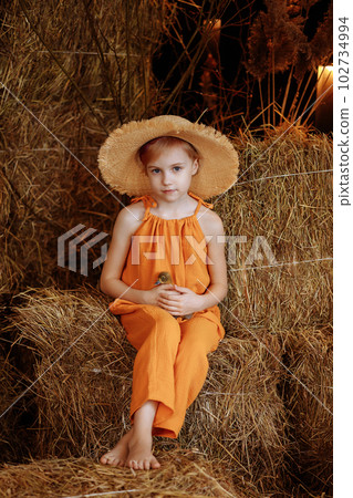 Child girl in an orange suit and a straw hat sits with a duck Child girl in an orange suit and a straw hat sits with a duck 102734994