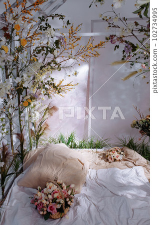 A bed in a bright bedroom surrounded by plants and flowers A bed in a bright bedroom surrounded by plants and flowers 102734995