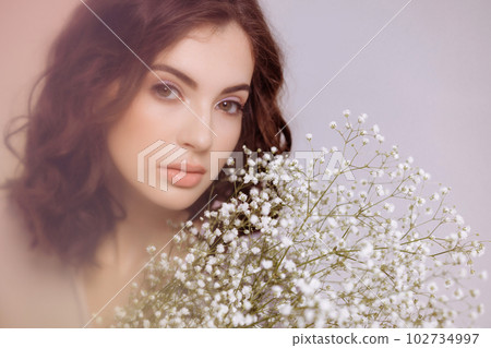A brunette girl holds a bouquet of gypsophila flowers in her hands. 102734997