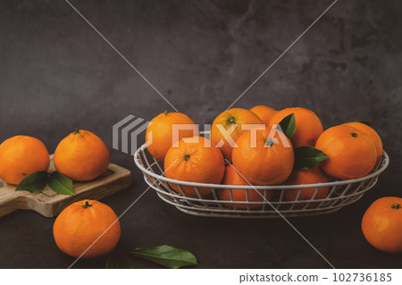 Orange fruit with green leaves on the Mandarin or Tangerine oranges in the basket on the stone table. Still life Orange fruit with green leaves on the Mandarin or Tangerine oranges in the basket on the stone table. Still life 102736185
