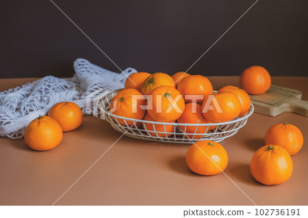 Mandarin or orange in the basket with fruit bag and wooden plate on the orange table top and black background. Mandarin or orange in the basket with fruit bag and wooden plate on the orange table top and black background. 102736191