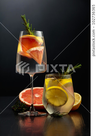 Gin tonic with ice, rosemary, lemon, and grapefruit on a black wooden table. 102736365