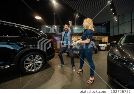 Happy married couple celebrating buying a car in a car showroom. Happy married couple celebrating buying a car in a car showroom. 102736721