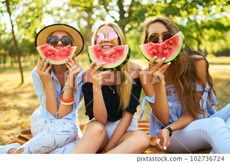 Three nice girls having fun eating watermelon In the park. Excellent sunny weather. Beautiful figures Three nice girls having fun eating watermelon In the park. Excellent sunny weather. Beautiful figures 102736724