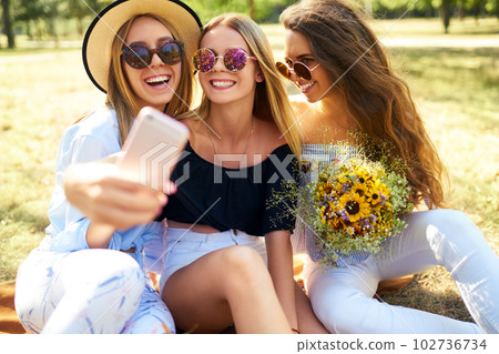 Three nice girls having fun In the park and make selfie. Excellent sunny weather. Beautiful figures. Three nice girls having fun In the park and make selfie. Excellent sunny weather. Beautiful figures. 102736734