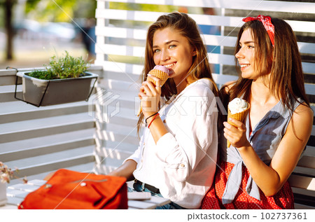 Two young female friends having fun and eating ice cream. Young women enjoy summer and vacation. Two young female friends having fun and eating ice cream. Young women enjoy summer and vacation. 102737361