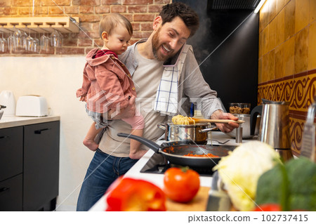 Multitasking father babysitting, cooking breakfast and talking on smart phone at home. 102737415