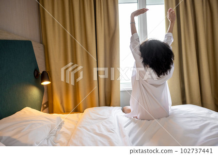 Pretty curly-haired woman in white bathrobe in a hotel in the morning Pretty curly-haired woman in white bathrobe in a hotel in the morning 102737441