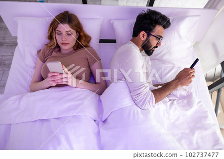 Wife and husband in bed using phones ignoring each other. 102737477