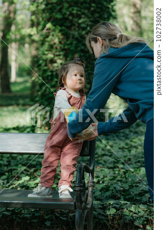 A female toddler in velvet overall is on the bench with her mother. 102738002