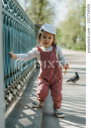A female toddler walks near the garden bridge fence. 102738009