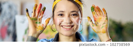 Portrait of excited young woman in apron smiling and showing her hands in paint at camera while creating abstract painting at home studio workshop Portrait of excited young woman in apron smiling and showing her hands in paint at camera while creating abstract painting at home studio workshop 102738569