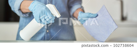 Close up shot of female hands in rubber gloves using detergent spray and cloth while cleaning kitchen surface Close up shot of female hands in rubber gloves using detergent spray and cloth while cleaning kitchen surface 102738604