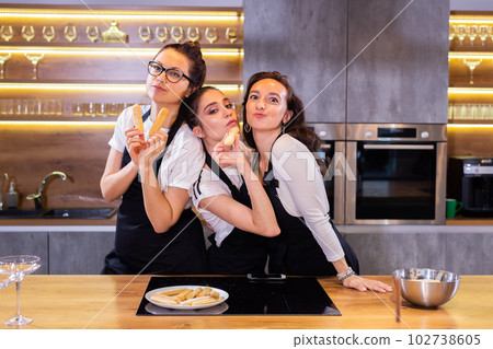 Three funny female chef in uniform holding cookies while smiling and having fun at camera in the kitchen Three funny female chef in uniform holding cookies while smiling and having fun at camera in the kitchen 102738605