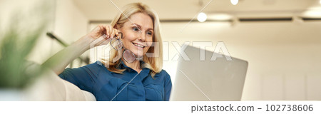 Cheerful mature businesswoman working from home, having online video call using laptop while sitting on a couch in modern apartment Cheerful mature businesswoman working from home, having online video call using laptop while sitting on a couch in modern apartment 102738606