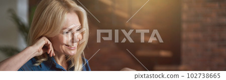 Smiling mature woman watching video using digital tablet pc, relaxing on a couch at home in the living room 102738665