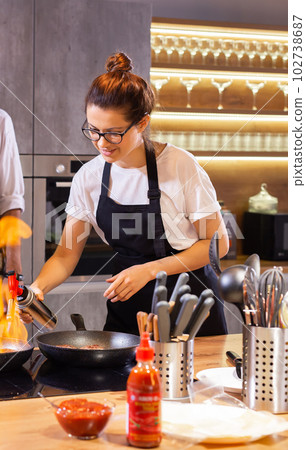 Female Chef in restaurant kitchen at stove with pan doing flambe on food Female Chef in restaurant kitchen at stove with pan doing flambe on food 102738687
