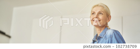 Attractive mature woman in rubber gloves smiling away, ready for clean up in the kitchen. Detergents, sanitizer spray and gel in bottle on the surface 102738709