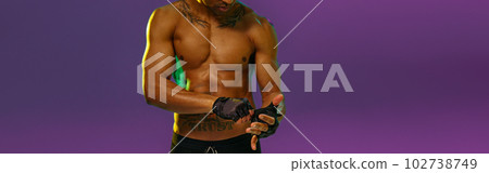 Portrait of muscular man puts on fighting gloves posing on studio background with color filter 102738749