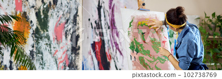 Back view of talented female artist working on a modern abstract oil painting. She is applying paint on canvas with fingers, standing in home studio workshop Back view of talented female artist working on a modern abstract oil painting. She is applying paint on canvas with fingers, standing in home studio workshop 102738769