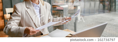 Businesswoman in glasses working with documents and use laptop while sitting in cafe near window Businesswoman in glasses working with documents and use laptop while sitting in cafe near window 102738797