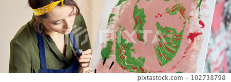 Creative young woman occupied in painting abstract picture, applying paint on canvas with fingers, standing in living room at home studio 102738798