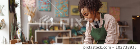 Smiling woman decorator making green ikebana on tray with epoxy resin in florist workshop 102738933