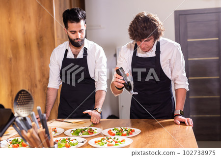 Chef pouring dressing over caprese salad in restaurant kitchen Chef pouring dressing over caprese salad in restaurant kitchen 102738975