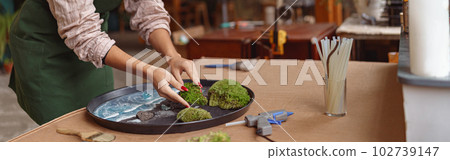 Woman decorator making green ikebana on tray with epoxy resin in florist workshop 102739147
