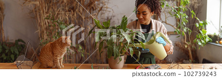 Smiling woman florist taking care of plant watering it in floral shop 102739243
