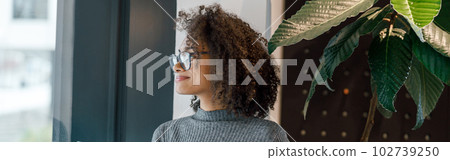 African businesswoman holding laptop and looking at side while standing near window in coworking African businesswoman holding laptop and looking at side while standing near window in coworking 102739250